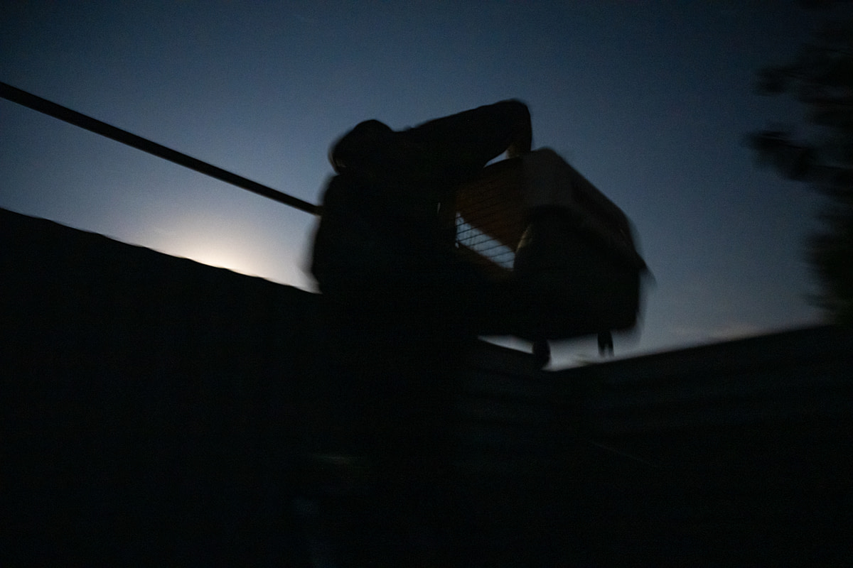 An investigator wearing a biohazard suit carefully climbs over a tall fence to exit a fur farm while holding a heavy carrying crate containing a rescued raccoon dog. Poland, 2024. Jo-Anne McArthur / Otwarte Klatki / We Animals An investigator wearing a biohazard suit carefully climbs over a tall fence to exit a fur farm while holding a heavy carrying crate containing a rescued raccoon dog. Poland, 2024. Jo-Anne McArthur / Otwarte Klatki / We Animals