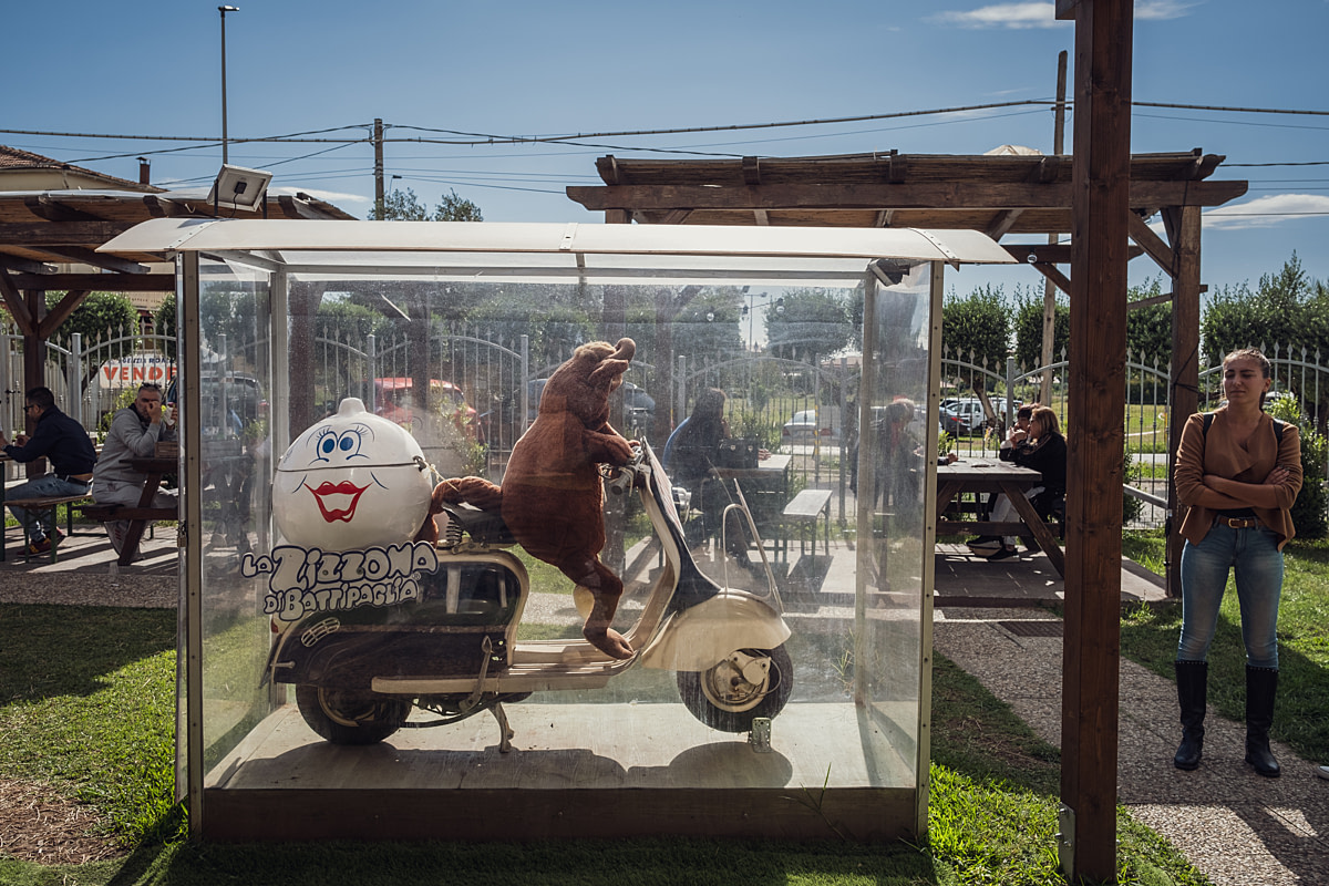The mascot of the buffalo mozzarella brand "La Zizzona" and a plush toy cow sit on a motor scooter in a display case in the company's Zizzona Village inner courtyard. "Zizzona" is Campanian dialect for "large breast." The Village is a food service area where the brand's products and other foods are sold. La Zizzona Dairy, Battipaglia, Salerno, Italy, 2024. Raffaele Petralla / We Animals