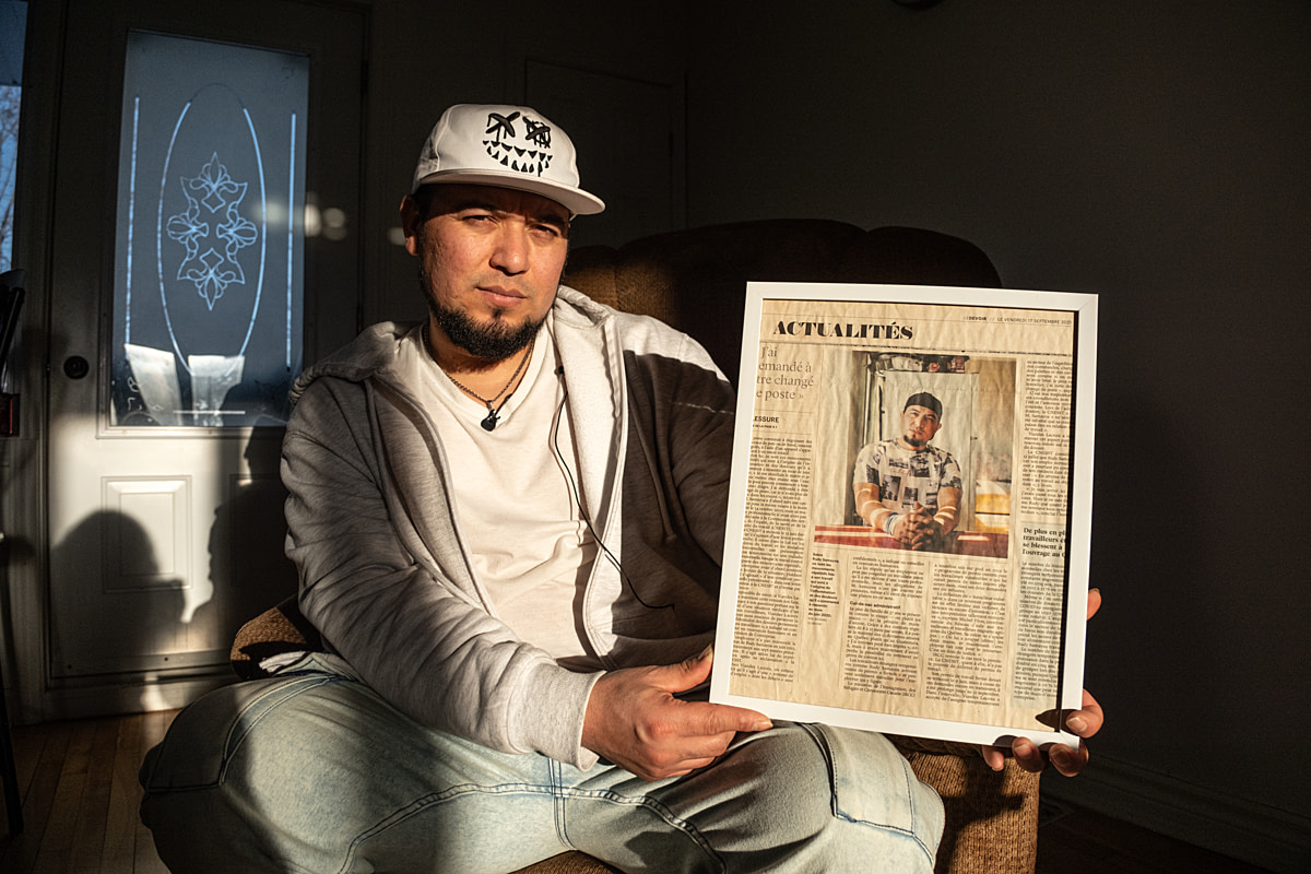 Rudy Samayoa, a former slaughterhouse worker, holds a framed copy of a news article outlining his experiences navigating the immigration system after he suffered an injury caused by his work. Undisclosed location, Sainte-Hyacinthe, Quebec, Canada, 2025. Ira Moon / We Animals