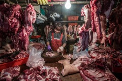Vendor chops pig carcasses and hangs on display for sale at a wet market in Taipei. Taiwan, 2019.
