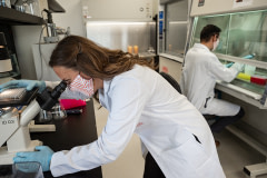 TurtleTree's Scientific Affairs Liaison, Vanessa Castagna, looks through a microscope while Head of Product, Ignacio Vargas, works in the background.
