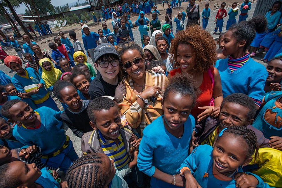 L-R: A Well-Fed World Founder Dawn Moncrief, IFA Founder Seble Nebiyeloul, and IFA School Health and Nutrition Program Coordinator Nardos Alemayehv, surrounded by children at a school outside Addis Ababa where IFA plant-based lunch programs are delivered.