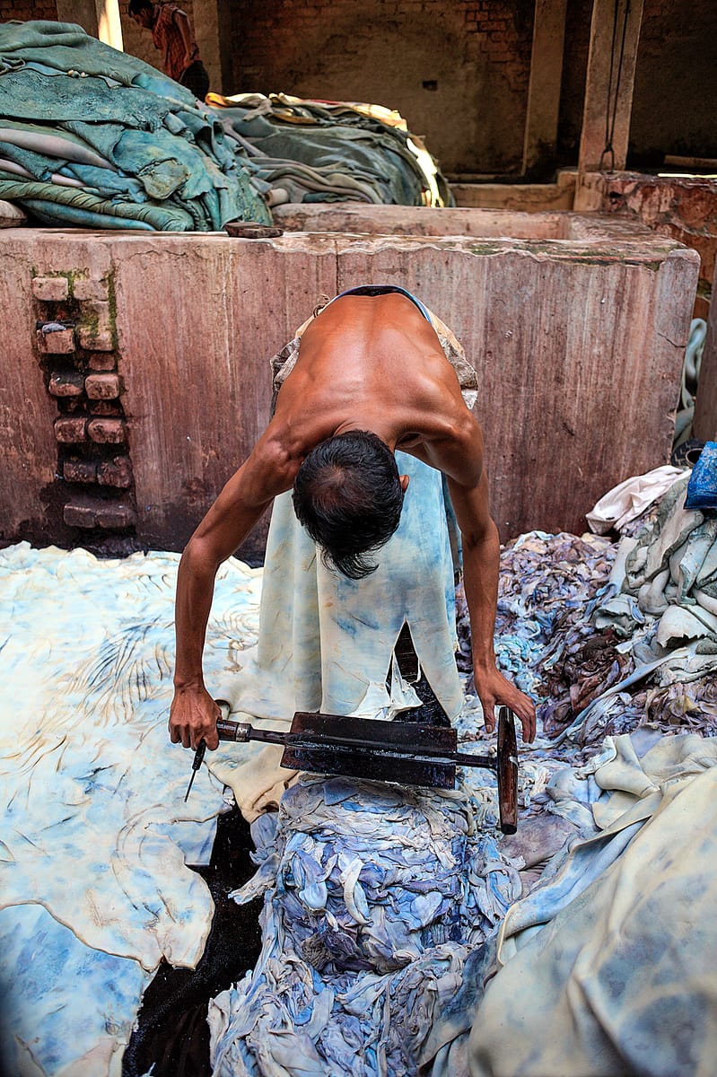 In Hazaribagh, a part of western Dhaka reknowned for its tanneries,  a worker bends over a cow hide. Using a specially formed knive, he removes the chemically dissolved layer of fat from the skin. Bangladesh, 2015. Christian Faesecke / We Animals Media