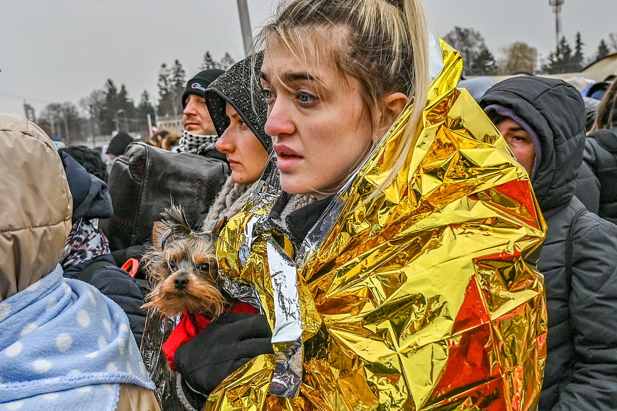 A Ukrainian refugee holds her small dog tightly against her chest as she waits in line at the reception center in Medyka on the Polish Ukrainian Border. An emergency blanket is wrapped around her shoulders to help her stay warm from the bitter winter cold. Poland, 2022. Miloš Bičanski / We Animals Media