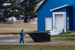 An inspector from the Canadian Food Inspection Agency (CFIA) walks towards a barn at a large duck farm wearing a full biohazard suit. A team of two was onsite at this facility in Racine, Quebec taking samples to test for the highly pathogenic avian influenza (H5N1). Canada, 2022. Victoria de Martigny / We Animals Media