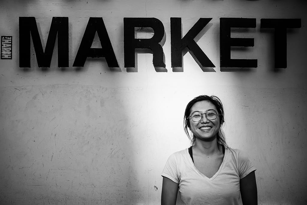 Jah Ying Chung, a food researcher in China, stands at the entrance to a wet market. Jah Ying is the co-founder of The Good Growth Co., which researches Chinese consumers' attitudes toward food and works in the plant-based/alternative protein and animal welfare spaces. Hong Kong, China, 2022. #unboundproject / We Animals Media