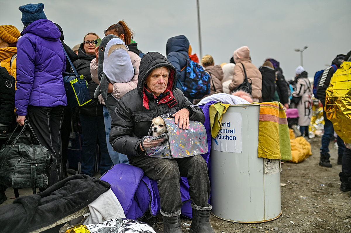 A man sits with his small dog on his lap at the reception center in Medyka on the Polish Ukrainian Border. The Ukrainian refugee is cold, hungry and exhausted after fleeing his home with only what he could carry. Poland, 2022. Miloš Bičanski / We Animals Media