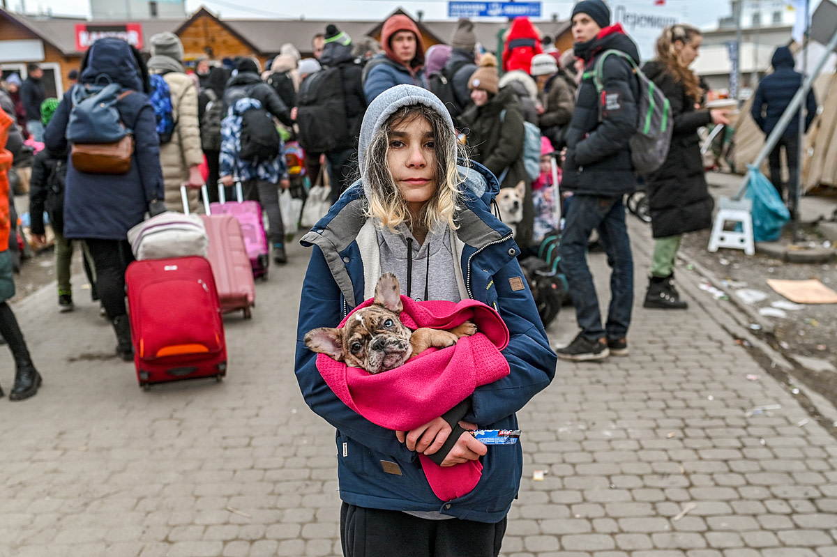 A young Ukrainian refugee carries her beloved dog in her arms as she waits at the Ukrainian Polish border in Medyka, Poland. Forced to flee her home with only what she could carry, she chose her dog. Poland, 2022. Miloš Bičanski / We Animals Media