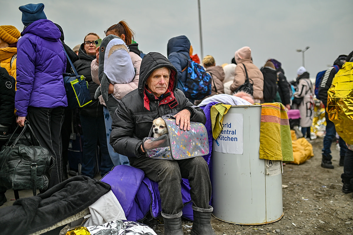A man sits with his small dog on his lap at the reception center in Medyka on the Polish Ukrainian Border. The Ukrainian refugee is cold, hungry and exhausted after fleeing his home with only what he could carry. Poland, 2022. Milos Bicanski / We Animals Media