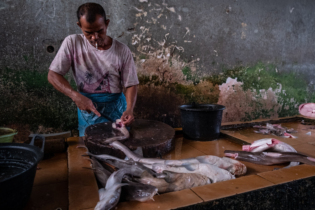 At a traditional Indonesian market, a worker butchers a shark, removing the animal's fins and separating them from the rest of the shark's flesh.