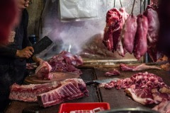 Vendor chops slabs of meat and hangs them for sale at a wet market in Taipei. Taiwan, 2019.