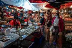 Shoppers browse the stalls at a wet market in Thailand in the early morning. A fish stall displays fish and shellfish.