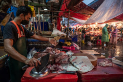 A butcher chops up cuts of pork behind the shop and out of the pouring rain at a wet market in Thailand.