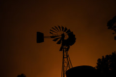 A windmill still stands with the orange night sky lit by the Caldor Fire behind it.