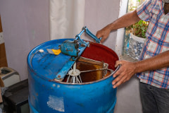 A honey producer turns a honey extractor machine's crank to extract honey from the frames sitting inside. 