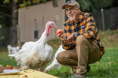 Tofurky founder Seth Tibbott and rescued turkeys enjoy a meal and each other's company at Wildwood Farm Sanctuary & Preserve. USA, 2021. Jo-Anne McArthur / We Animals Media