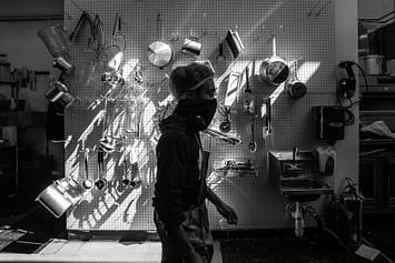 Chef walks by a wall of kitchen utensils at Baltimore's vegan restaurant The Greener Kitchen. Photo by: Jo-Anne McArthur / #UnboundProject / We Animals Media.