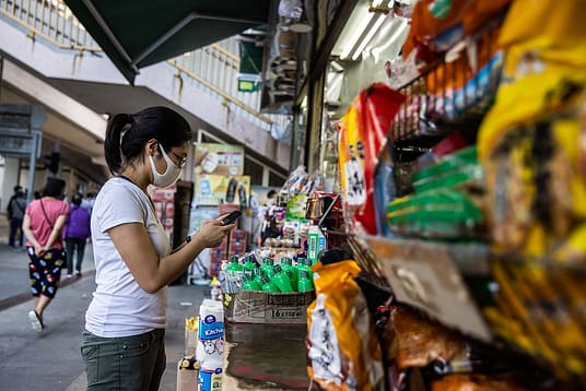 Jah Ying Chung, a food researcher in China, uses her mobile device outside an urban grocery store. Jah Ying is the co-founder of The Good Growth Co., which researches Chinese consumers' attitudes toward food and works in the plant-based/alternative protein and animal welfare spaces. Hong Kong, China, 2022. #unboundproject / We Animals Media
